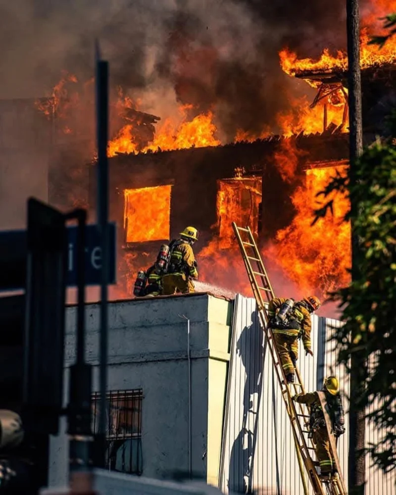 Firefighters and a ground ladder beside a burning structure.